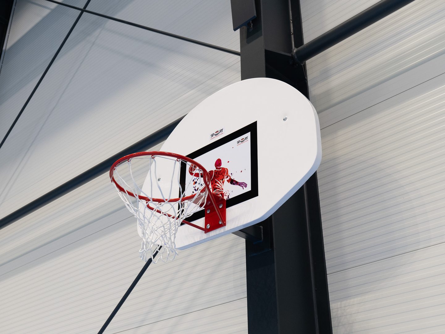 Detail basketbalového koše s deskou a síťkou proti stropní konstrukci.