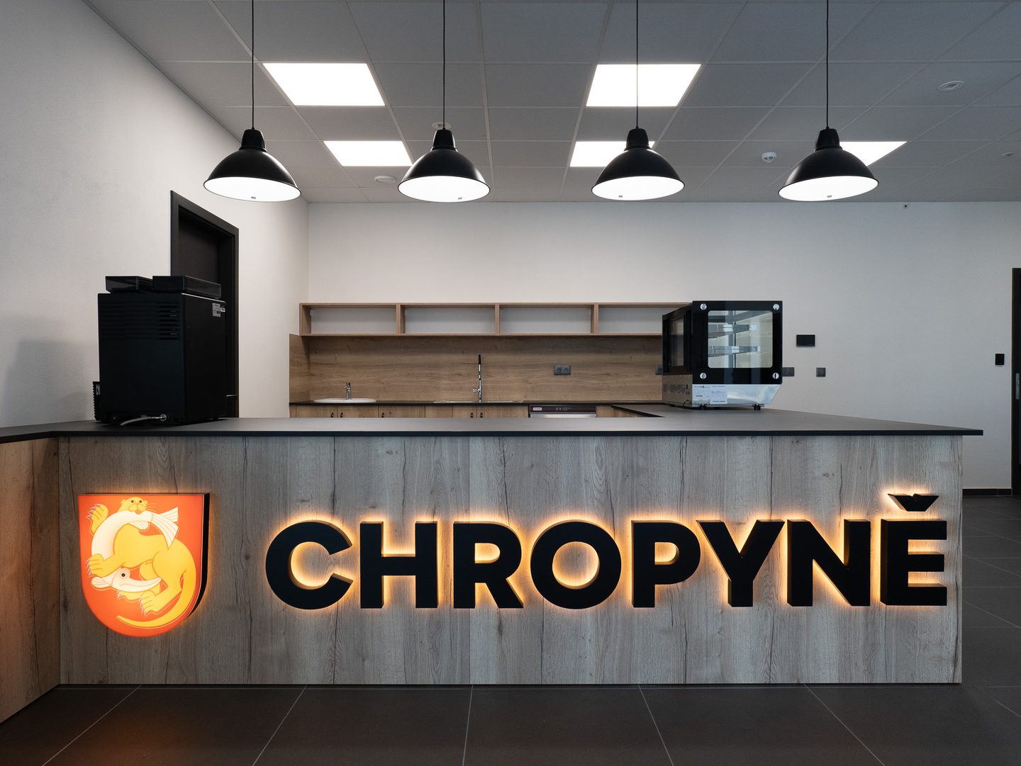 Bufet s dřevěným pultem a podsvíceným znakem města Chropyně.