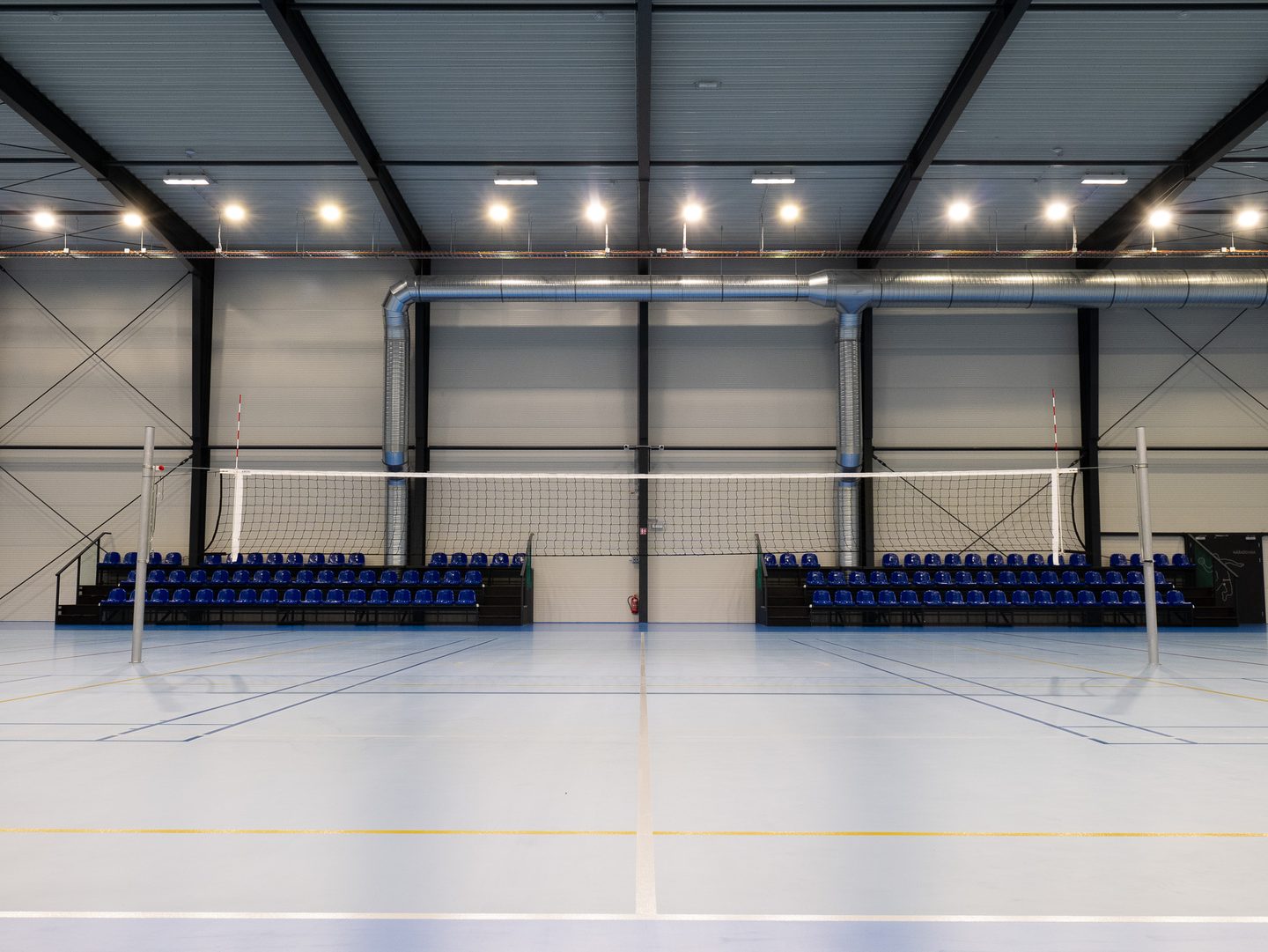 Rozestavěné volejbalové sítě přes hrací plochu, za nimi modrá tribuna.