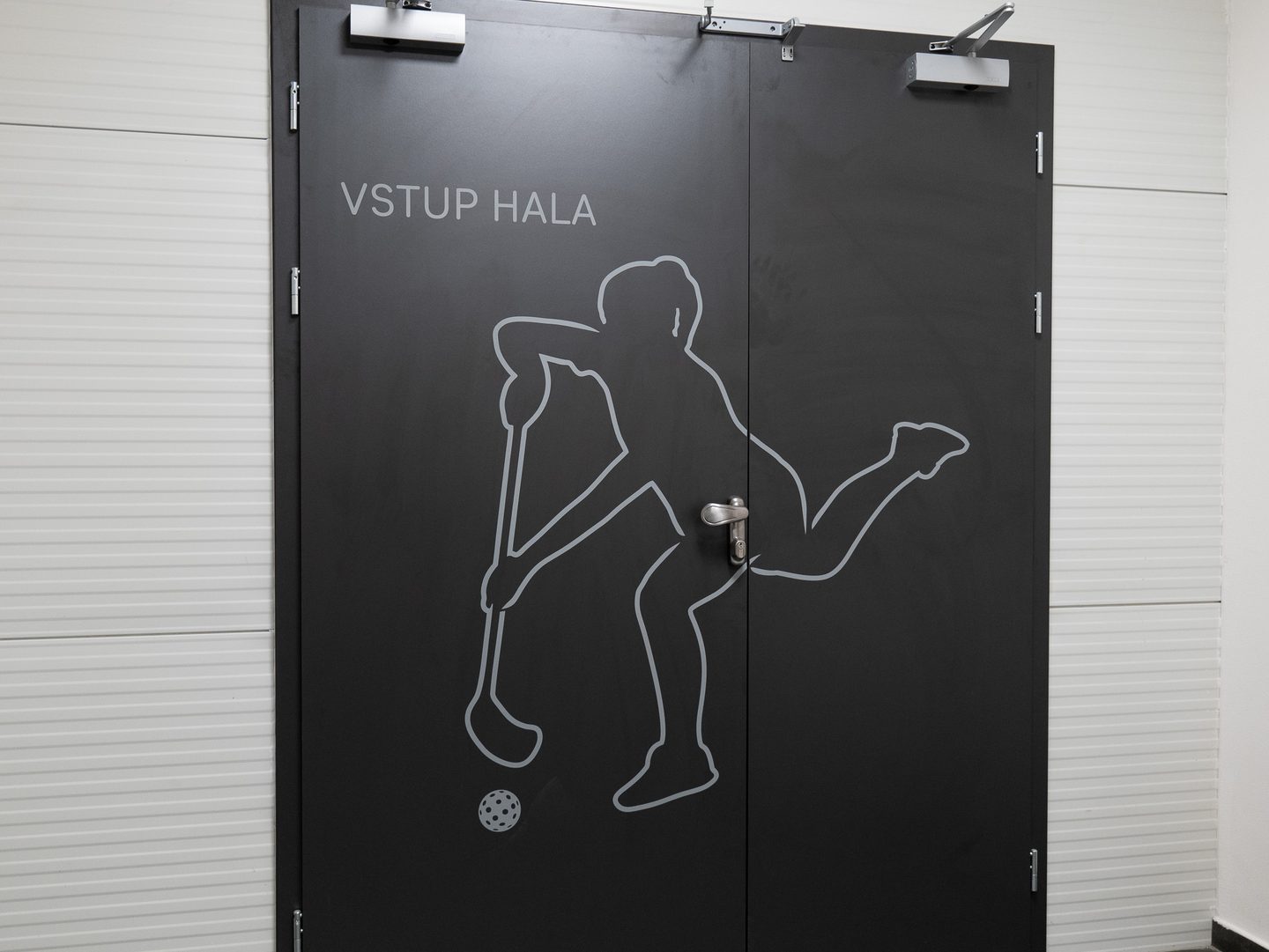 Tmavé dveře s nápisem VSTUP HALA a bílou siluetou fotbalisty.