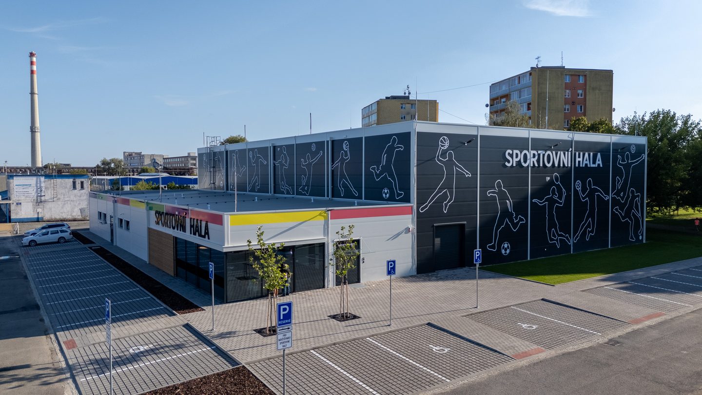 Boční pohled na halu s dlouhou fasádou pokrytou siluetami sportovců.