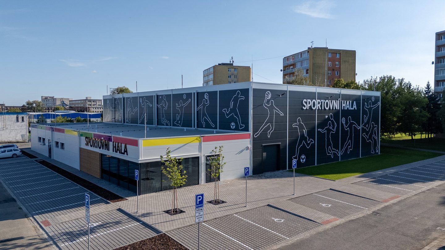 Hala a parkoviště s vyznačenými stáními, v pozadí sídliště.